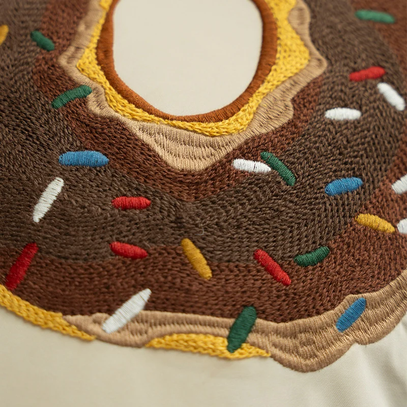 Quadratisches Dekokissen mit gesticktem Donut-Motiv und dekorativer Kederkante
